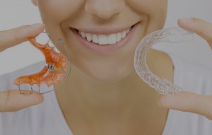 Smiling woman holding retainer and Invisalign tray