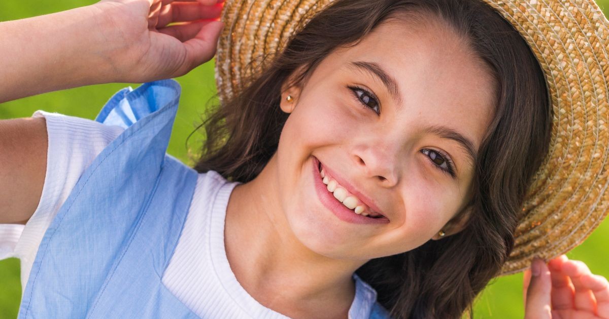 little girl in straw hat smiling for a blog post titled: does my child need an orthodontist